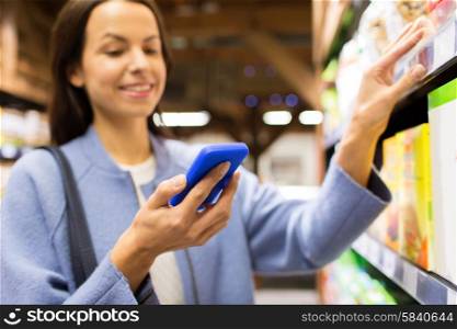 sale, shopping, consumerism and people concept - happy young woman with smartphone choosing and buying food in market