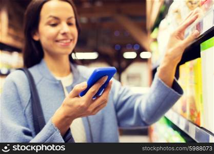 sale, shopping, consumerism and people concept - happy young woman with smartphone choosing and buying food in market