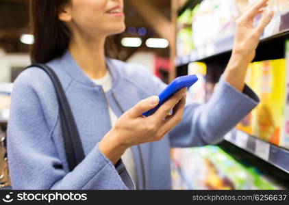 sale, shopping, consumerism and people concept - happy young woman with smartphone choosing and buying food in market