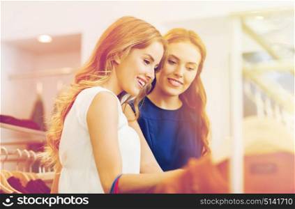 sale, shopping, consumerism and people concept - happy young women choosing clothes at clothing shop. happy women choosing clothes at clothing shop