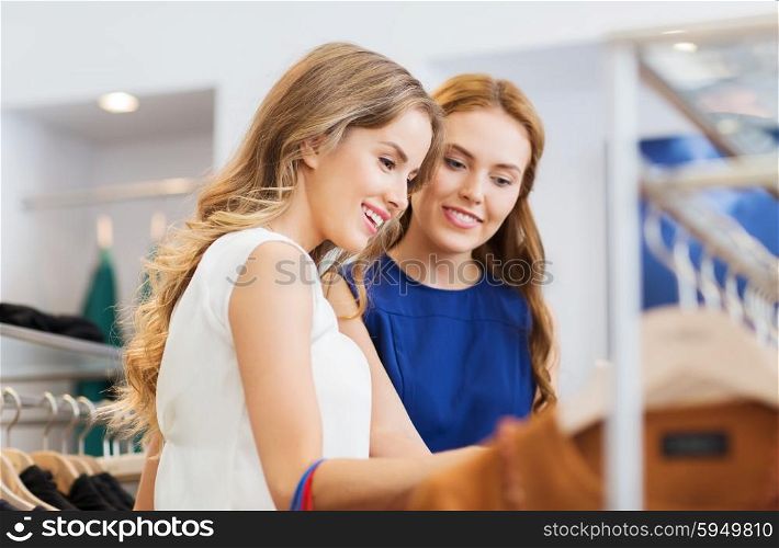 sale, shopping, consumerism and people concept - happy young women choosing clothes at clothing shop
