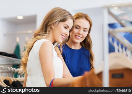 sale, shopping, consumerism and people concept - happy young women choosing clothes at clothing shop
