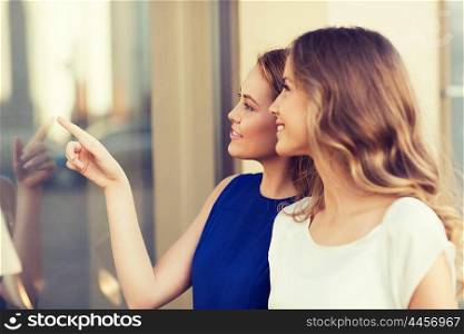sale, shopping, consumerism and people concept - happy young women pointing finger to shop window outdoors