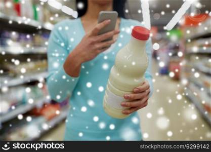 sale, shopping, consumerism and people concept - young female customer with smartphone holding milk bottle at grocery store or supermarket over snow. customer with smartphone and milk at supermarket