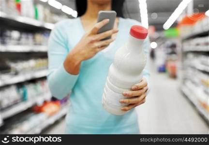 sale, shopping, consumerism and people concept - young woman with smartphone holding milk bottle at grocery store or supermarket. woman with smartphone buying milk at supermarket. woman with smartphone buying milk at supermarket