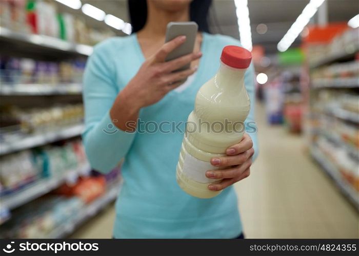 sale, shopping, consumerism and people concept - young woman with smartphone holding milk bottle at grocery store or supermarket