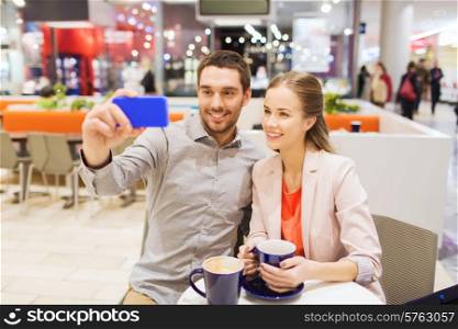 sale, shopping, consumerism, technology and people concept - happy young couple with smartphone taking selfie at cafe in mall