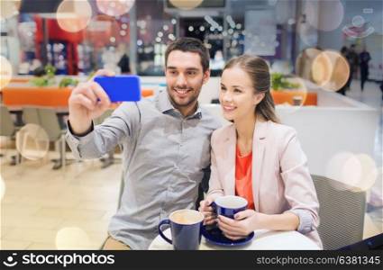 sale, shopping, consumerism, technology and people concept - happy young couple with smartphone taking selfie at cafe in mall. happy couple with smartphone taking selfie in mall