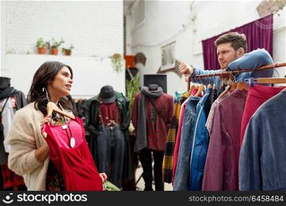 sale, shopping, fashion and people concept - couple choosing clothes at vintage clothing store and showing thumbs down. couple choosing clothes at vintage clothing store