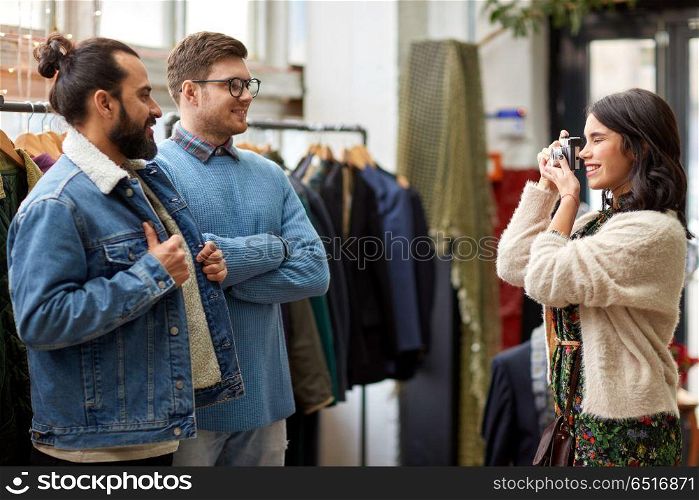 sale, shopping, fashion and people concept - friends choosing clothes and photographing by film camera at vintage clothing store. friends photographing at vintage clothing store. friends photographing at vintage clothing store