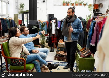 sale, shopping, fashion and people concept - friends choosing clothes at vintage clothing store and showing like or dislike. friends choosing clothes at vintage clothing store