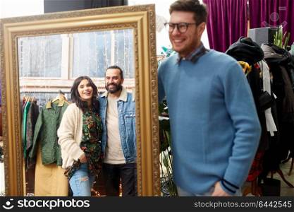sale, shopping, fashion and people concept - happy smiling friends looking at mirror reflection at vintage clothing store. happy friends at mirror at vintage clothing store