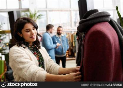 sale, shopping, fashion and people concept - happy young woman choosing clothes at clothing store. happy woman choosing clothes at clothing store
