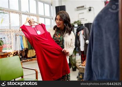 sale, shopping, fashion and people concept - happy young woman choosing dress at clothing store. happy woman choosing dress at clothing store