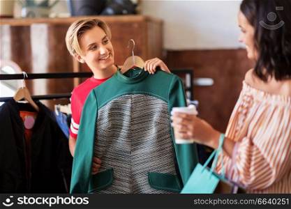 sale, shopping, fashion and people concept - happy young women with coffee choosing clothes at vintage clothing store. women choosing clothes at vintage clothing store