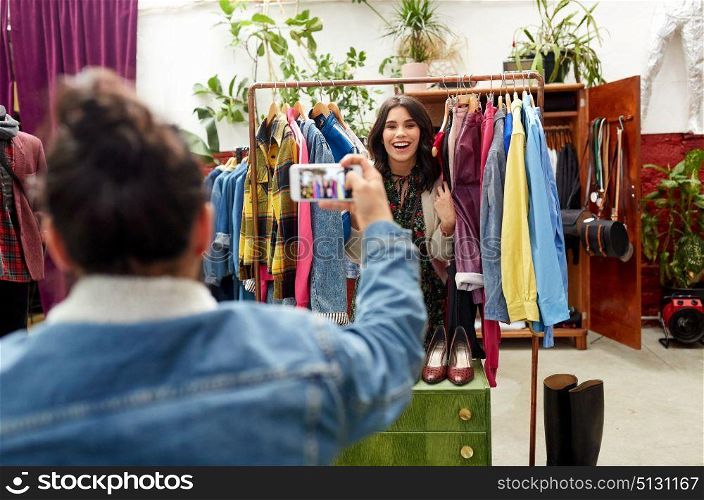 sale, shopping, fashion and people concept - man photographing happy woman by smartphone at vintage clothing store hanger. happy couple photographing at clothing store. happy couple photographing at clothing store