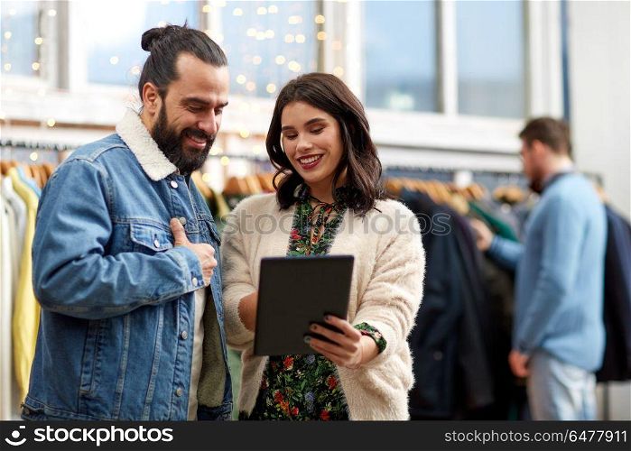 sale, shopping, fashion and technology concept - happy couple with tablet pc computer choosing clothes at vintage clothing store. couple with tablet pc at vintage clothing store. couple with tablet pc at vintage clothing store