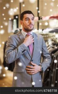 sale, shopping, fashion, business style and people concept - elegant young man choosing and trying on suit and tie in mall or clothing store over snow