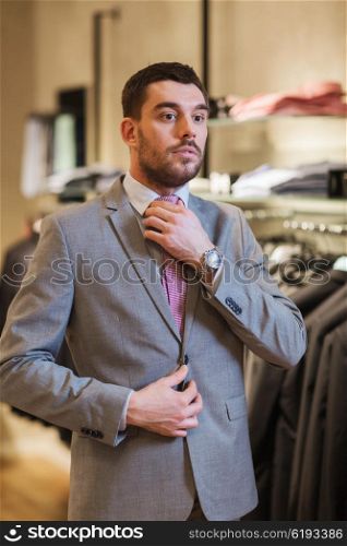 sale, shopping, fashion, business style and people concept - elegant young man choosing and trying on suit and tie in mall or clothing store