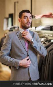 sale, shopping, fashion, business style and people concept - elegant young man choosing and trying on suit and tie in mall or clothing store