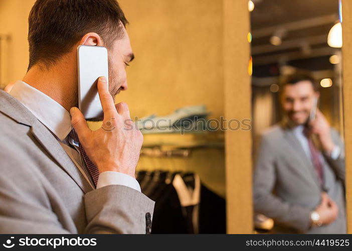 sale, shopping, fashion, communication and people concept - close up of young man calling on smartphone and and looking to mirror at clothing store