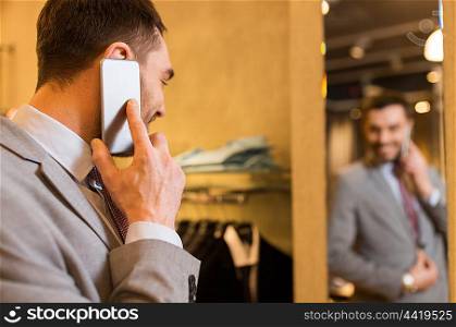 sale, shopping, fashion, communication and people concept - close up of young man calling on smartphone and and looking to mirror at clothing store