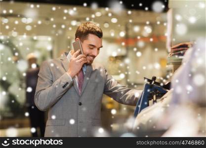 sale, shopping, fashion, communication and people concept - happy young man calling on smartphone and choosing clothes at clothing store over snow