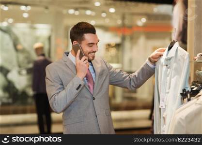 sale, shopping, fashion, communication and people concept - happy young man calling on smartphone and choosing clothes at clothing store