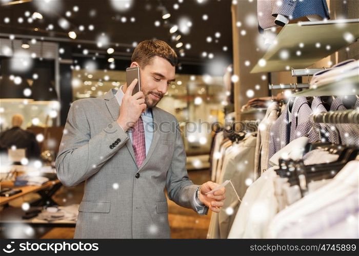 sale, shopping, fashion, communication and people concept - happy young man or businessman calling on smartphone and choosing clothes at clothing store over snow
