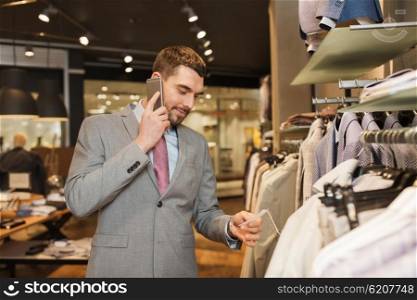 sale, shopping, fashion, communication and people concept - happy young man or businessman calling on smartphone and choosing clothes at clothing store