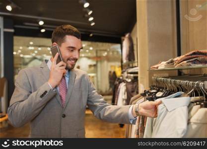 sale, shopping, fashion, communication and people concept - happy young man or businessman calling on smartphone and choosing clothes at clothing store