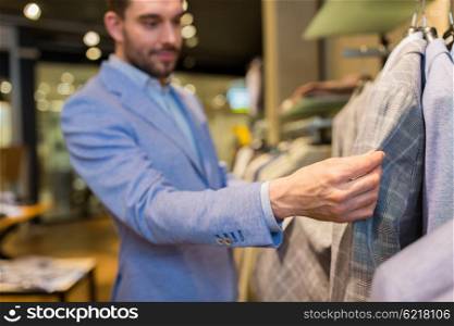 sale, shopping, fashion, style and people concept -close up of happy young man in suit choosing clothes in mall or clothing store