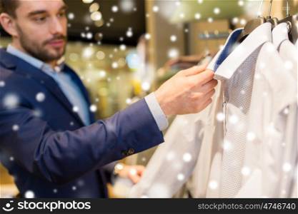 sale, shopping, fashion, style and people concept - close up of young man in suit choosing shirt in mall or clothing store over snow