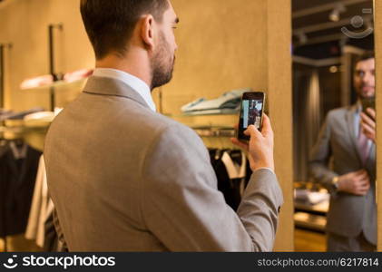 sale, shopping, fashion, style and people concept - close up of young man in suit with smartphone taking mirror selfie at clothing store