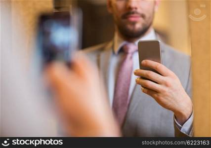 sale, shopping, fashion, style and people concept - close up of young man in suit with smartphone taking mirror selfie at clothing store
