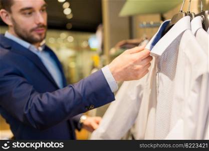 sale, shopping, fashion, style and people concept - close up of young man in suit choosing shirt in mall or clothing store