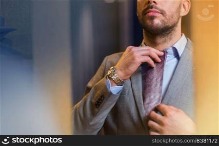 sale, shopping, fashion, style and people concept - close up of young man in suit choosing and trying tie on and looking to mirror in mall or clothing store. close up of man trying tie on at mirror