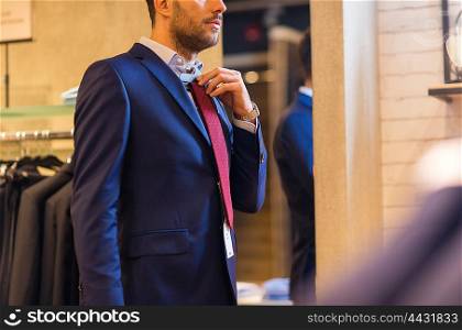 sale, shopping, fashion, style and people concept - elegant young man choosing and trying tie on at clothing store