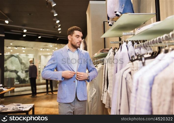 sale, shopping, fashion, style and people concept - elegant young man choosing and trying jacket on in mall or clothing store