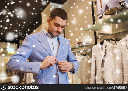 sale, shopping, fashion, style and people concept - elegant young man choosing and trying jacket on in mall or clothing store over snow