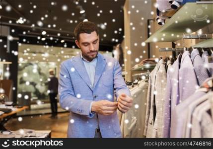 sale, shopping, fashion, style and people concept - elegant young man choosing and trying jacket on in mall or clothing store over snow