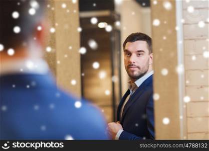 sale, shopping, fashion, style and people concept - elegant young man choosing and trying jacket on and looking to mirror in mall or clothing store over snow