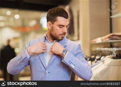 sale, shopping, fashion, style and people concept - elegant young man choosing and trying jacket on in mall or clothing store