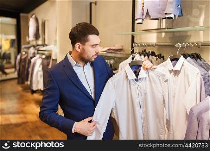 sale, shopping, fashion, style and people concept - elegant young man in suit choosing shirt in mall or clothing store