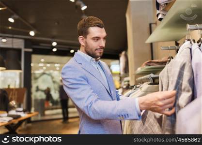 sale, shopping, fashion, style and people concept - elegant young man in jacket choosing clothes in mall or clothing store