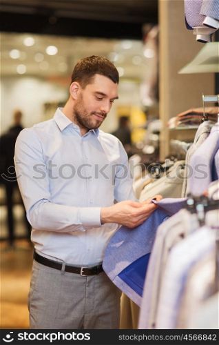 sale, shopping, fashion, style and people concept - elegant young man in shirt choosing clothes in mall or clothing store