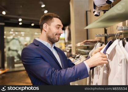 sale, shopping, fashion, style and people concept - elegant young man in suit choosing clothes in mall or clothing store