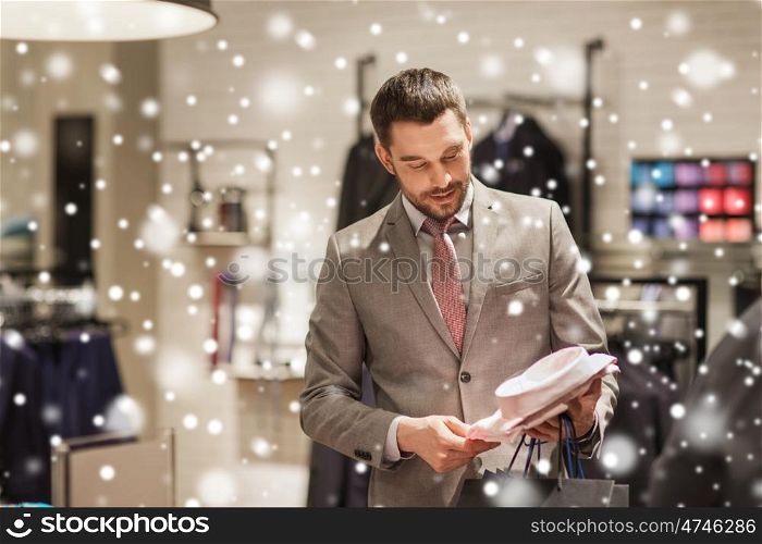 sale, shopping, fashion, style and people concept - elegant young man in suit choosing shirt in mall or clothing store over snow