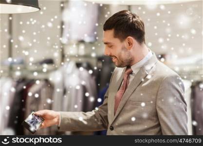 sale, shopping, fashion, style and people concept - elegant young man in suit choosing bow-tie in mall or clothing store over snow