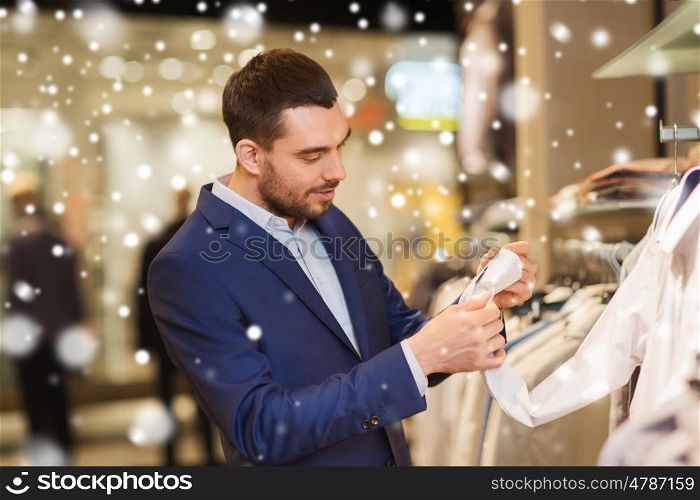 sale, shopping, fashion, style and people concept - elegant young man in suit choosing clothes in mall or clothing store over snow